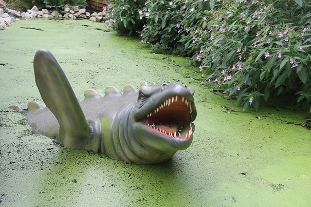 Green animatronic dinosaur with an open mouth in a pond.