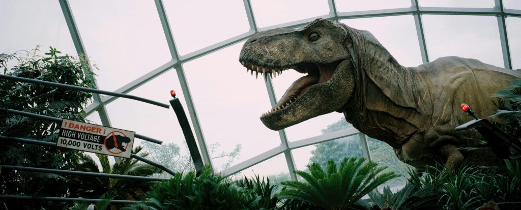 A dinosaur animatronic towering over trees and roaring.